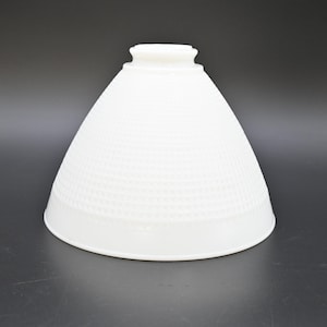 May include: A white, cone-shaped lampshade with a textured, dotted pattern. The lampshade has a wide base and a narrower top with a small, cylindrical opening. The shade is made of a solid, opaque material.