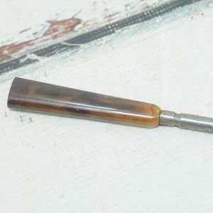 Op de afbeelding: Een metalen gereedschap met een lange, dunne schacht en een bruin en beige handvat.