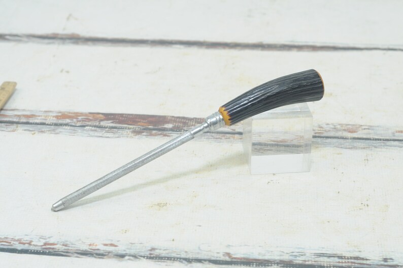 May include: A silver knife sharpener with a black and yellow handle. The handle is made of a textured material that resembles wood.