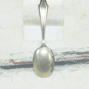 May include: A silver teaspoon with a simple, elegant design. The spoon has a rounded bowl and a long, slender handle.