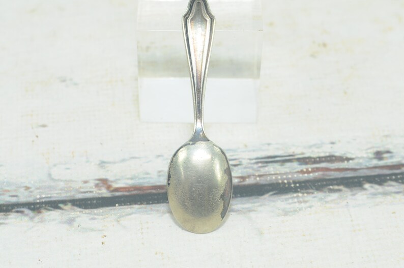 May include: A silver teaspoon with a simple, elegant design. The spoon has a rounded bowl and a long, slender handle.