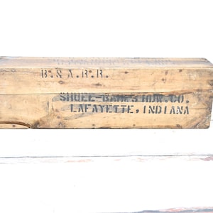 May include: A rectangular wooden crate with visible wood grain. The crate has black stenciled text that reads "B & A.R.R." and "SHUEE-BARNES IRON CO. LAFAYETTE, INDIANA". The crate is aged and weathered.