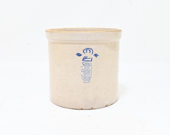 Könnte beinhalten: Ein zylindrischer, beigefarbener Steinguttopf mit flachem Rand. Auf der Vorderseite befindet sich ein blauer Stempelaufdruck des Bundesstaates Illinois mit dem Text "Western Stoneware Co. Monmouth, Ill." und einer blauen Ziffer 2 über dem Umriss.