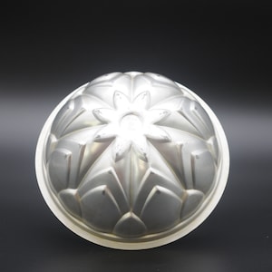May include: Silver-colored metal cake pan with a decorative flower design. The pan has a round shape and a smooth, shiny surface.