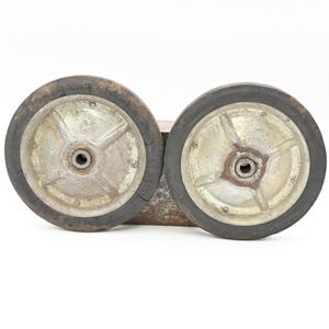 May include: Two vintage metal wheels with black rubber tires. The wheels are attached to a rusty metal frame. The wheels have a silver center with a star-shaped design and a central hub.