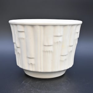 May include: Cream-coloured ceramic plant pot with a textured, vertical bamboo-like pattern. The pot has a wide, slightly flared shape and a raised base. The neutral colour and unique texture make it versatile for various decor styles.
