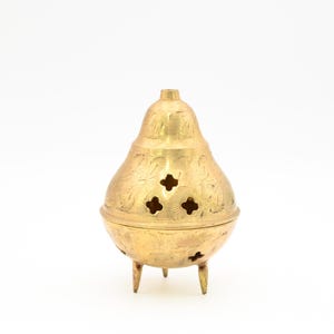 May include: A gold metal incense burner with intricate floral designs and four small holes. The burner has three legs and a pear-shaped body.