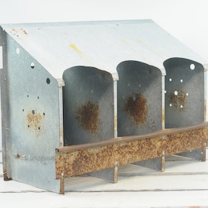 May include: A vintage metal chicken coop with three nesting boxes. The coop is made of galvanized metal and has a rusty patina. The coop has a slanted roof and a small perch.