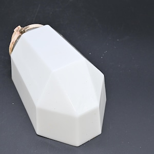 Op de afbeelding: Een wit, geometrisch gevormd object met een goudkleurige bovenkant. Het object heeft een facetontwerp, met meerdere platte oppervlakken die een kristalachtige uitstraling creëren. Het item staat tegen een donkere achtergrond.