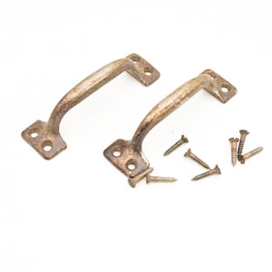 May include: Two antique bronze-colored cabinet handles with mounting plates and curved grips. Several matching screws are scattered nearby. The hardware has a weathered, vintage appearance, suggesting age and use.