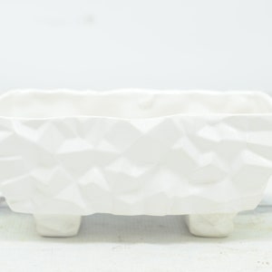 以下が含まれることがあります： しわくちゃの紙のような質感の白いセラミック製のプランター。プランターは短い脚が4本あり、小さな植物に最適です。