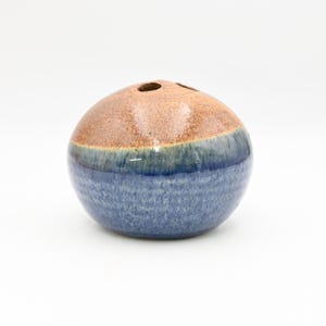 May include: A spherical ceramic vase with a speckled brown top, a green band, and a textured blue base. The vase has three small openings on top. This decorative vase is suitable for small floral arrangements.