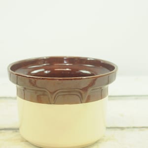 May include: A brown and cream glazed ceramic planter with a rounded rim and a slightly flared base.