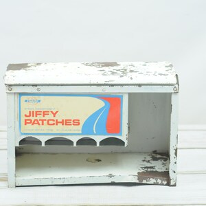 May include: White metal box with a Jiffy Patches label. The box has a shelf with five slots and is slightly rusted.