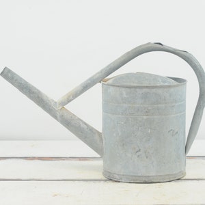 May include: A silver metal watering can with a long spout and a handle. The can has a worn, rustic look.