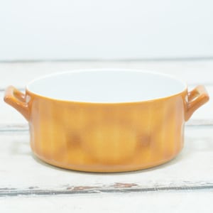 Può includere: Una ciotola in ceramica marrone con due manici. La ciotola ha un interno bianco e un esterno testurizzato.