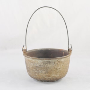 May include: A small, gray cast iron pot with a wire handle. The pot has a rustic, aged look.