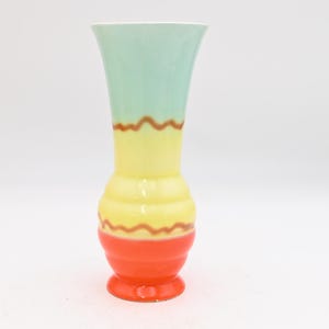 May include: A colorful ceramic vase with a flared top. The top is light green, transitioning to yellow, then orange at the base. Brown wavy lines separate the colors. The vase has a round base and a white interior.