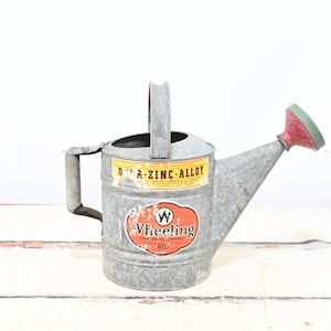 Könnte beinhalten: Vintage Gießkanne aus verzinktem Stahl mit rotem und grünem Ausguss. Die Kanne hat einen Griff und einen Seitengriff. Die Kanne hat zwei Etiketten, eines mit der Aufschrift "D-A-ZINC-ALLOY" und eines mit der Aufschrift "Wheeling".