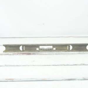 May include: A vintage metal level with a brass finish. The level has a single bubble and is marked with "CAST IRON" on the side.