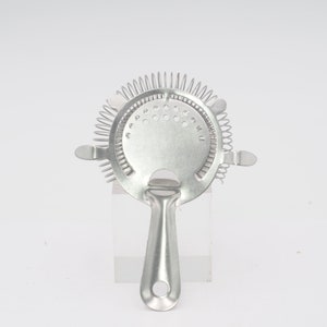 Puede incluir: Un colador de cóctel plateado con una espiral de resorte y un mango. El colador está diseñado para separar el hielo y otros sólidos de los cócteles.