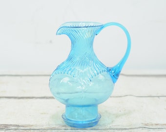 May include: A light blue glass pitcher with a textured design and a round base. The pitcher has a handle and a spout.