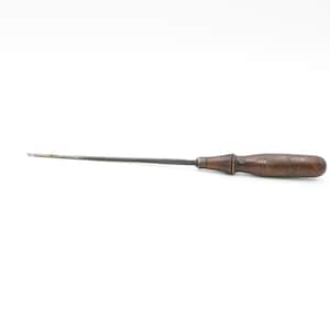 Puede incluir: Una herramienta de metal larga y delgada con un mango de madera. La herramienta se utiliza para raspar o limpiar.