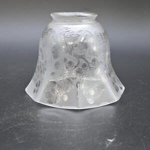 May include: Frosted glass lampshade with a flared, bell-like shape. The shade features an etched design of grapes and leaves, creating a vintage aesthetic. The clear glass allows light to pass through, illuminating the intricate pattern.