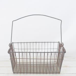 May include: A rusty metal wire basket with a single handle. The basket is empty and has a rectangular shape.