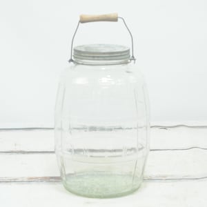 Peut inclure: Un bocal en verre transparent avec une poignée en bois et un couvercle en métal. Le bocal a une forme de tonneau avec des lignes en relief.