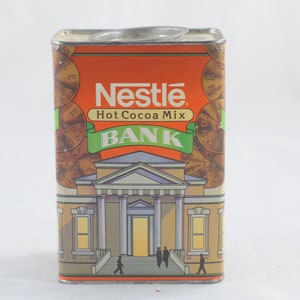 Pode incluir: Um cofre vintage de metal laranja e verde em forma de lata com o logotipo da Nestl&eacute; e as palavras "Hot Cocoa Mix Bank".