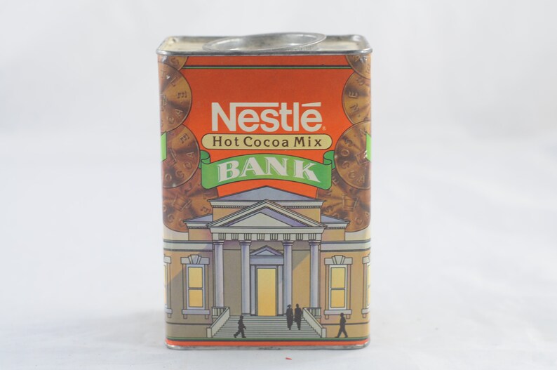 Pode incluir: Um cofre vintage de metal laranja e verde em forma de lata com o logotipo da Nestl&eacute; e as palavras "Hot Cocoa Mix Bank".
