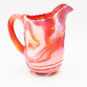 May include: A red and white swirl glass jug with a scalloped rim and a handle. The jug has a vintage look and is made of opaque glass.