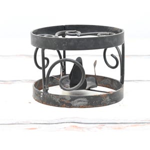 Puede incluir: Candelero de metal negro con un diseño decorativo de volutas. El candelero tiene una base redonda y una forma cilíndrica.