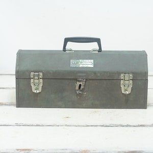 May include: A vintage green metal toolbox with a black plastic handle and silver latches. The toolbox has a label that reads "INDUSTRIAL" on the front.