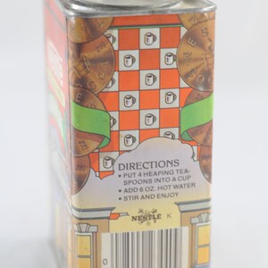 Pode incluir: Uma lata vintage para cacau Nestl&eacute;. A lata &eacute; laranja, verde e marrom com um padr&atilde;o xadrez e imagens de x&iacute;caras de ch&aacute;. O texto na lata diz "DIRECTIONS: PUT 4 HEAPING TEA-SPOONS INTO A CUP ADD 6 OZ. HOT WATER STIR AND ENJOY NESTLE K 28000 23440".
