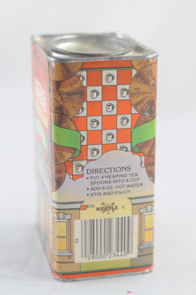Pode incluir: Uma lata vintage para cacau Nestl&eacute;. A lata &eacute; laranja, verde e marrom com um padr&atilde;o xadrez e imagens de x&iacute;caras de ch&aacute;. O texto na lata diz "DIRECTIONS: PUT 4 HEAPING TEA-SPOONS INTO A CUP ADD 6 OZ. HOT WATER STIR AND ENJOY NESTLE K 28000 23440".