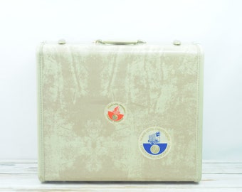 May include: A vintage beige suitcase with two travel stickers. One sticker is red and white and the other is blue and white. The blue and white sticker says "Hotel Motel Christchurch, International Airport, New Zealand".