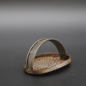 Puede incluir: Un rallador de metal vintage con un mango. El rallador tiene una forma rectangular y una superficie texturizada. El mango está hecho de metal y está unido al rallador con dos remaches.