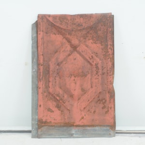 May include: A vintage metal tile with a geometric design. The tile is painted a rusty orange colour and has a silver border.
