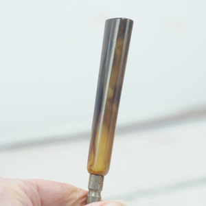 Op de afbeelding: Een bruine en gele gestreepte schroevendraaier met een metalen punt.