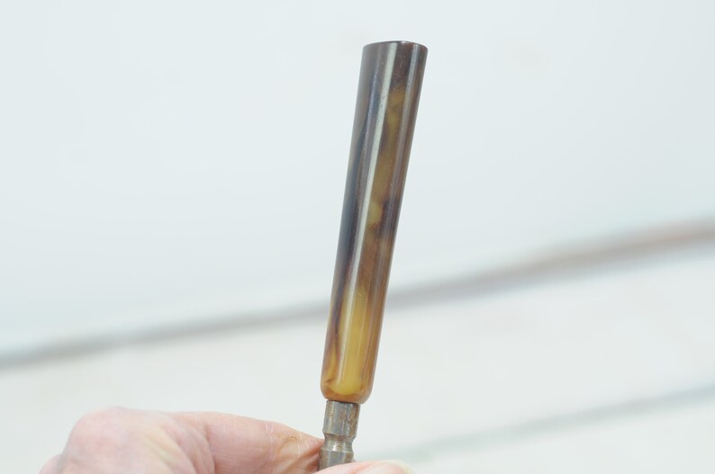 Op de afbeelding: Een bruine en gele gestreepte schroevendraaier met een metalen punt.