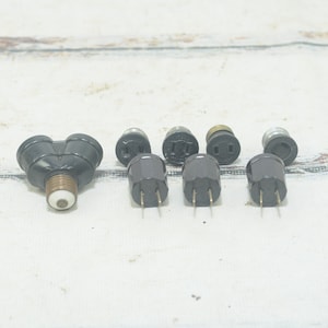 Puede incluir: Un conjunto de adaptadores eléctricos negros con dos clavijas. Hay tres adaptadores con dos clavijas y tres adaptadores con una clavija. Los adaptadores están sobre una superficie de madera blanca.
