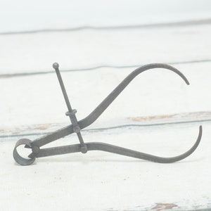 Pode incluir: Uma ferramenta de calibre vintage de metal com uma mandíbula arredondada em uma extremidade e uma mandíbula pontiaguda na outra. O calibre é feito de metal e tem um acabamento prateado.