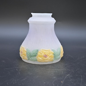 Może przedstawiać: Biały, matowy szklany klosz lampy o rozkloszowanym kształcie. Klosz ma pionowe żebrowane detale i jest ozdobiony żółtymi różami i zielonymi liśćmi wokół podstawy. Klosz jest przeznaczony do oprawy oświetleniowej.