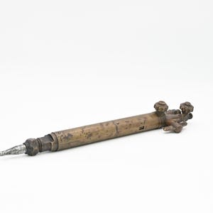 May include: A brass welding torch with two knobs and a long, thin nozzle.