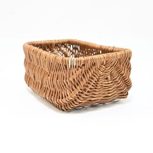 May include: A rectangular storage basket constructed from light brown woven material. The basket features a distinct chevron-like pattern created by the interlacing of the strands along the sides and corners, with an open top and a sturdy base.