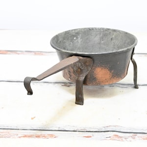 May include: A small copper pot with a handle and three legs. The pot is tarnished and has a rustic look.