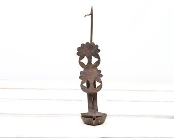 May include: A rustic metal candle holder with a decorative design. The holder has a small bowl at the bottom and two decorative pieces with cut-out designs above it.