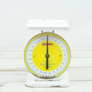 May include: A white vintage kitchen scale with a yellow face and black needle. The scale reads "The Victor" and "Weighs Pounds by Ounces".